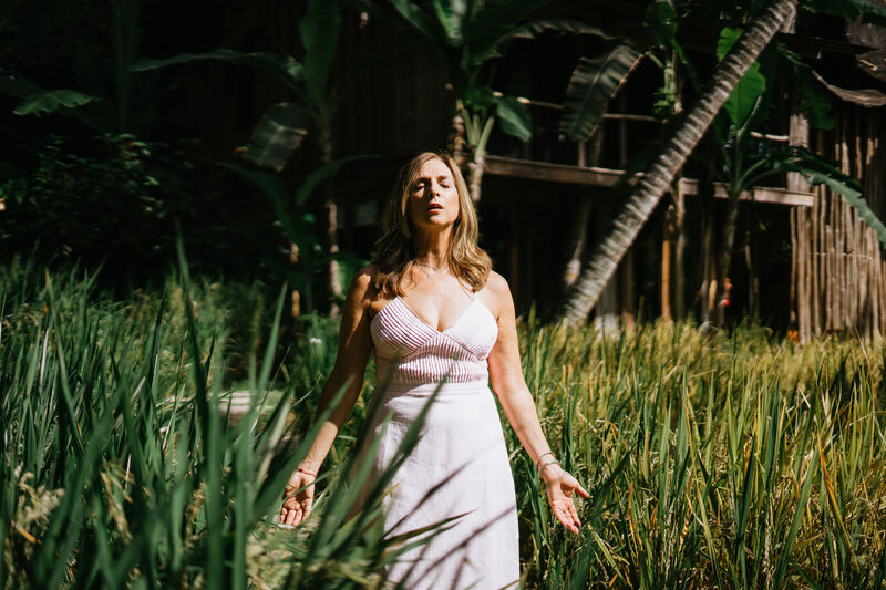 Julie Wright Halbert standing in tall grass, eyes closed, arms open at her sides